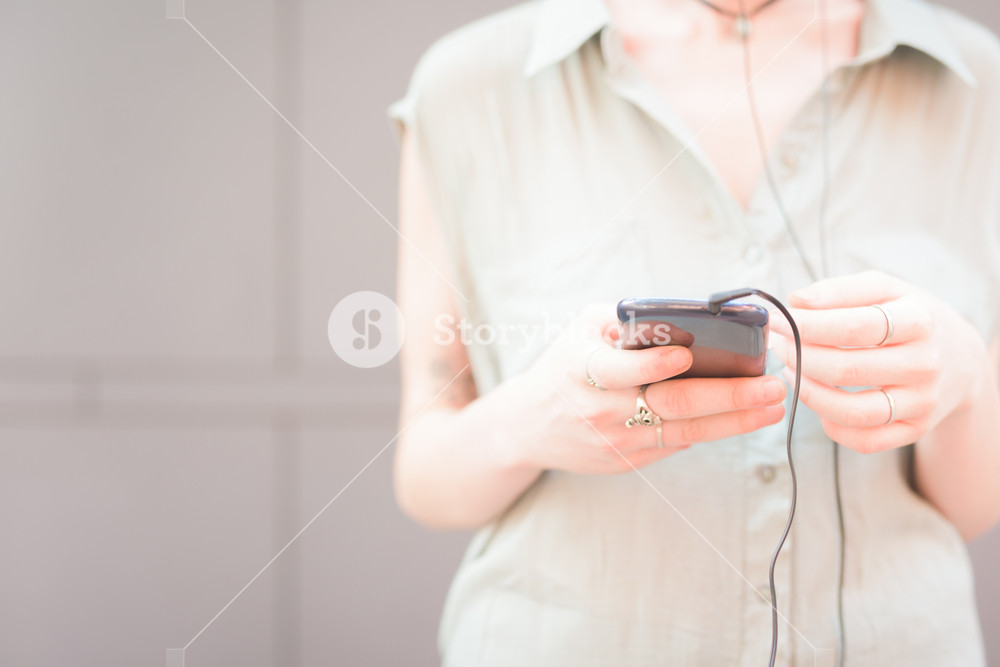 Close up on the hands of a woman holding a smartphone, listening music with headphones, tapping the screen - technology, music, communication concept