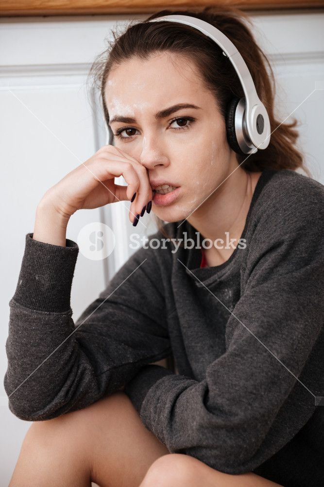 Close-up portrait of a somber young person enjoying music with earphones indoors