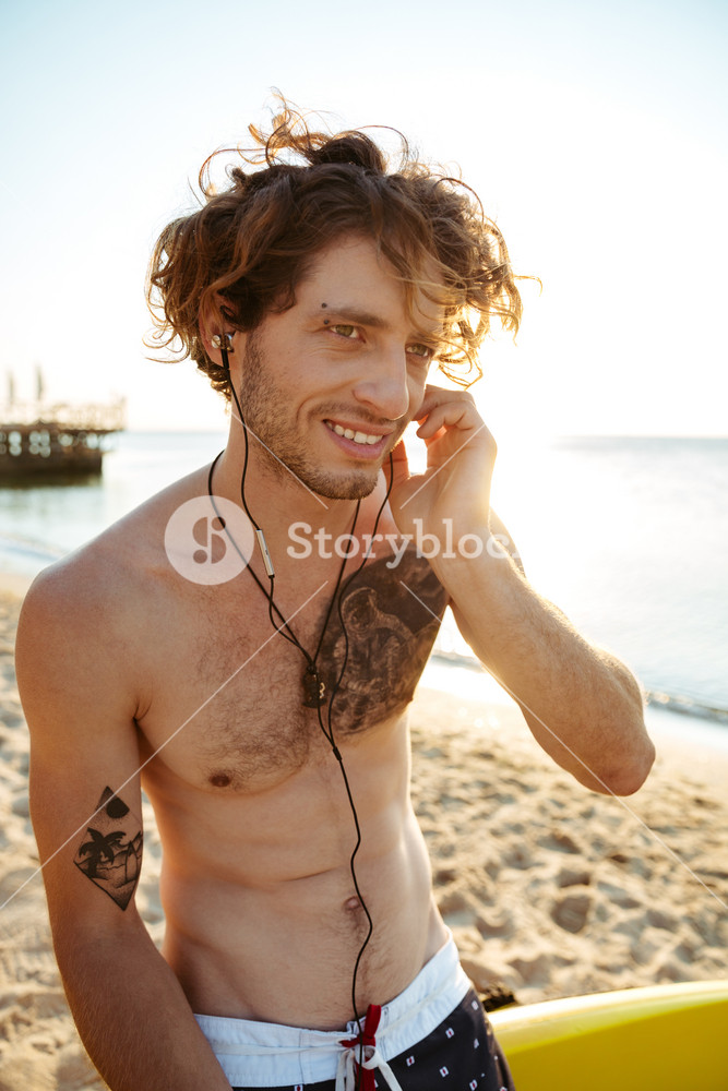 Portrait of a young surfer enjoying music on a surfboard at the beach