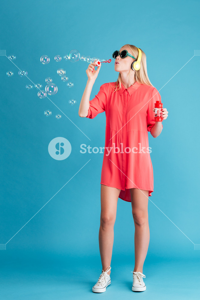 Portrait of a fashionable blonde woman blowing soap bubbles and listening to music