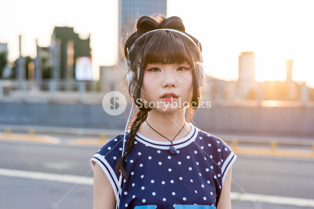 Young Asian woman listening to music outdoors in the city - serious, music, relax concept