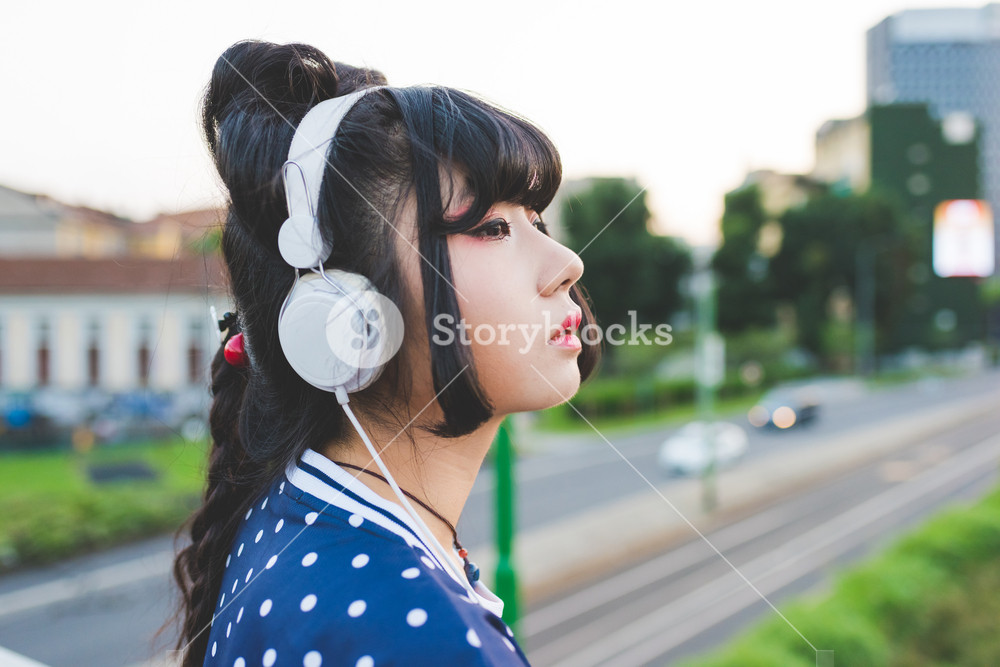 Young Asian woman listening to music outdoors, contemplating the future