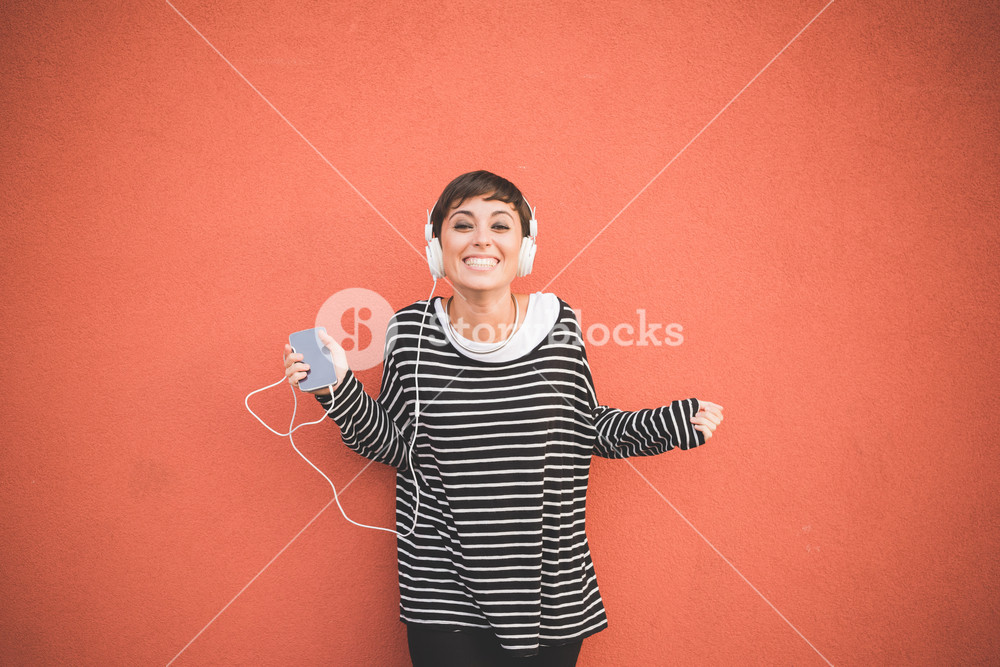 Young woman listening to music with headphones, smiling and holding smartphone - technology, music concept