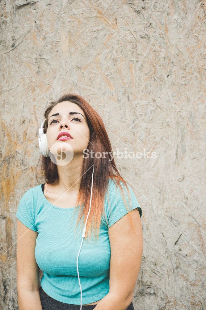 Young woman listening to music, deep in thought, against a wall