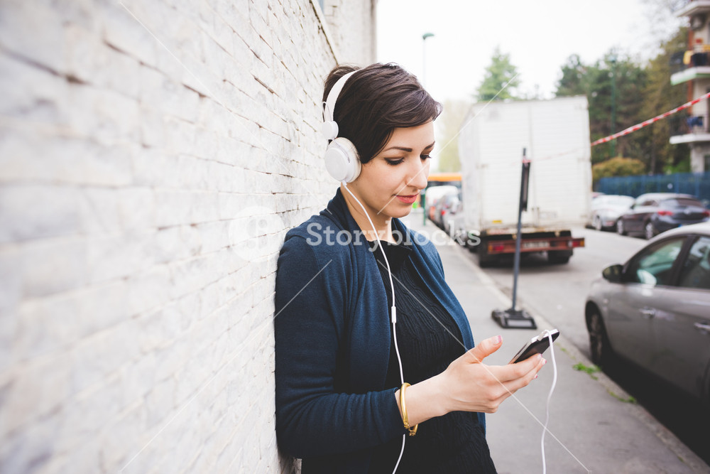 Half length profile portrait of young woman leaning against a wall, listening to music with headphones, eyes closed - serene, enjoying, music concept