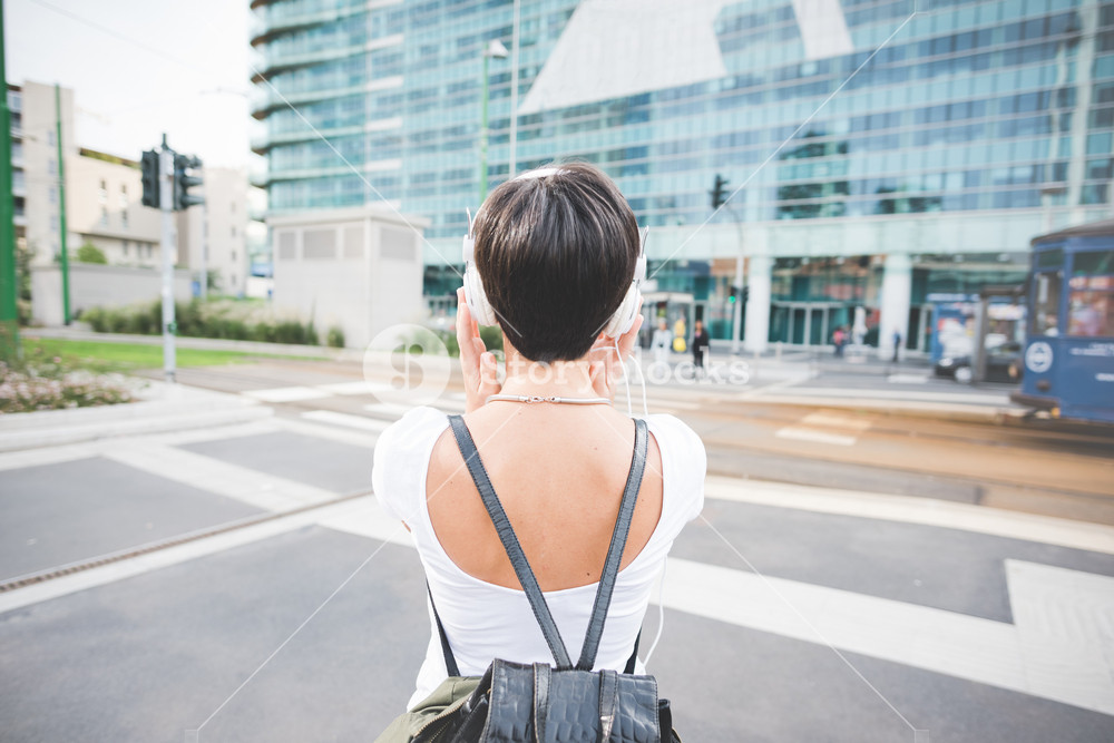 Half length rear view of a caucasian woman with backpack listening music with headphones - music, relax concept