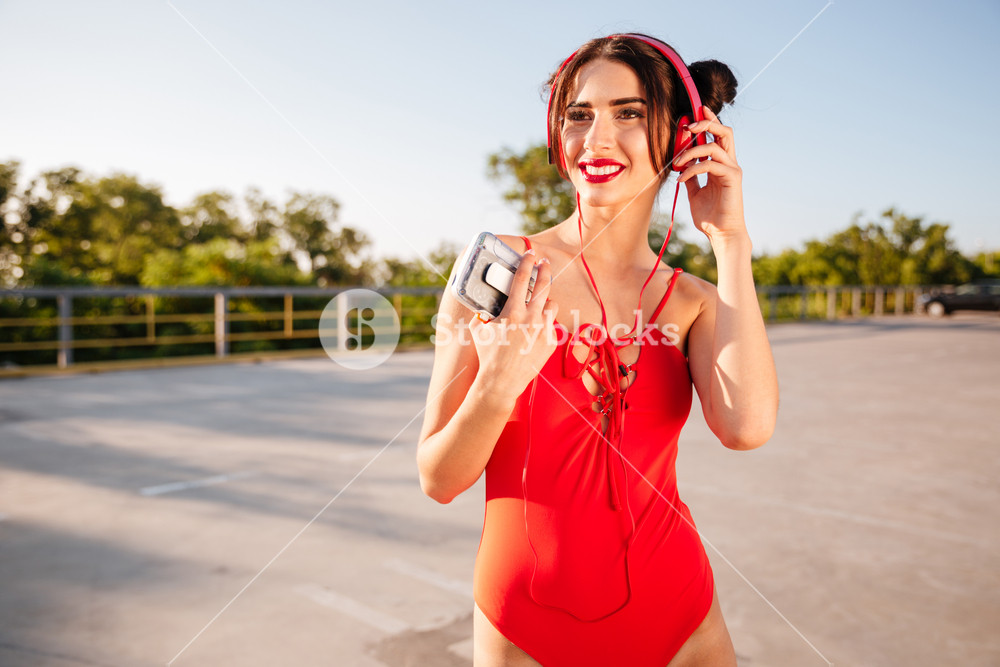 Joyful woman in red swimsuit enjoying music from vintage cassette player