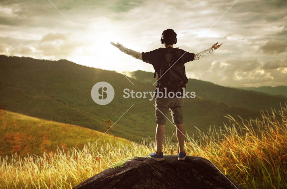 Hiker with backpack standing on top of a mountain with raised hands and ...