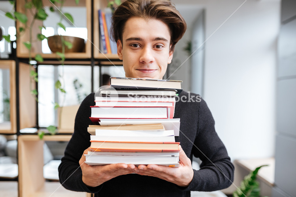 Image of cheerful student in library holding a lot of books. Look at ...