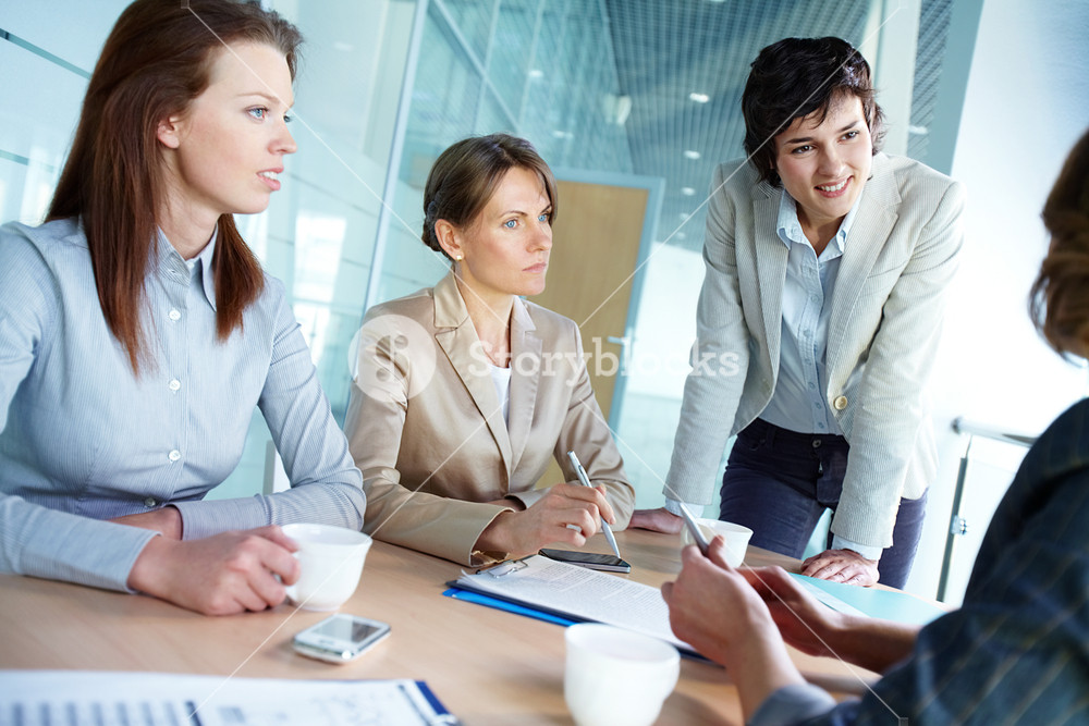 Image of three attentive businesswomen listening to their employer at meeting