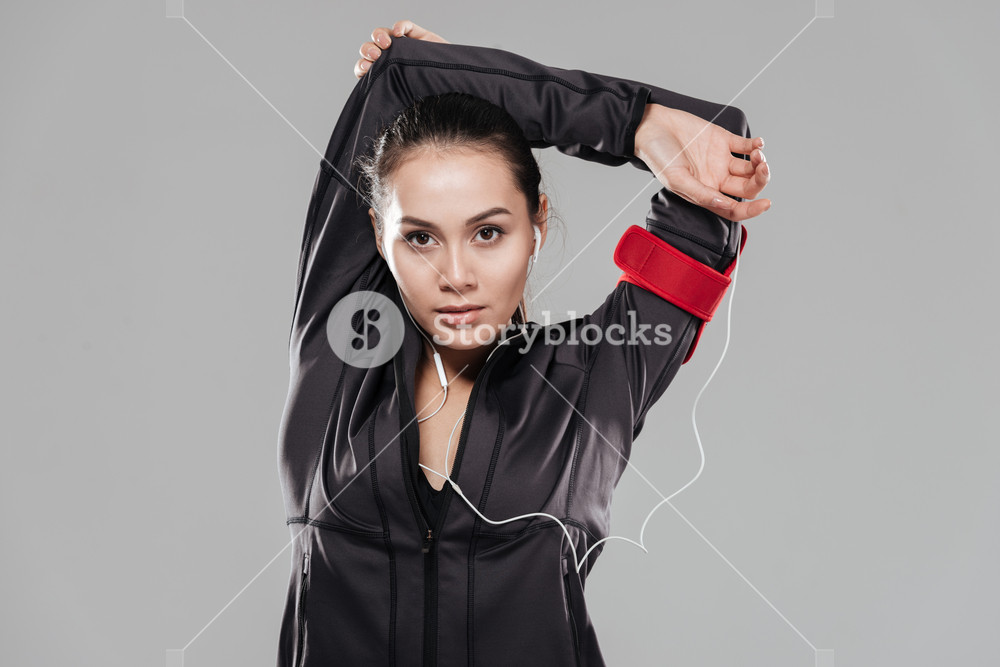 Young woman doing fitness exercises with earphones over grey background.