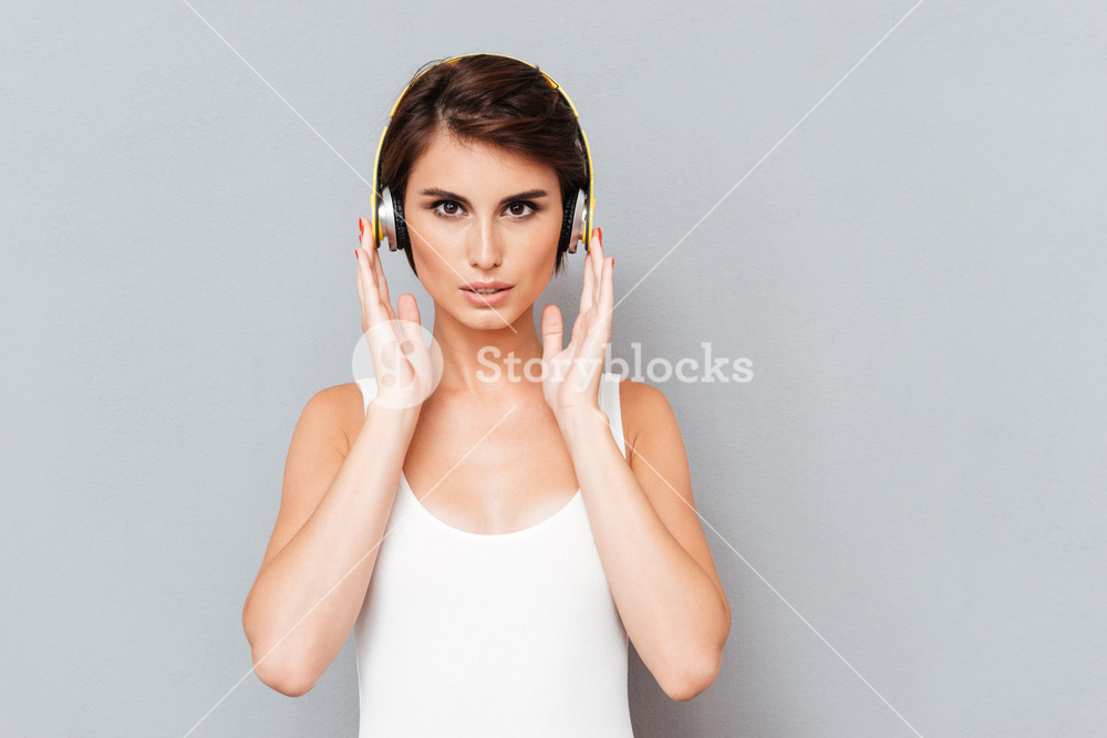 Portrait of a pensive concentrated woman listening music in headphones over gray background