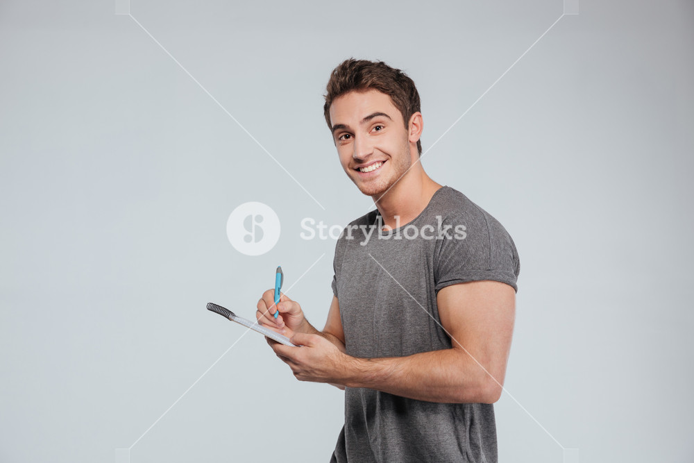Portrait of a smiling casual man making notes in notepad with pen and ...