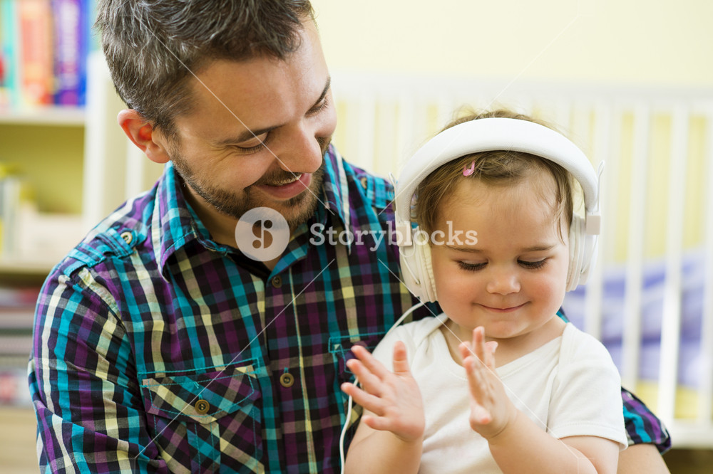 Portrait of joyful father and his young daughter enjoying music with headphones