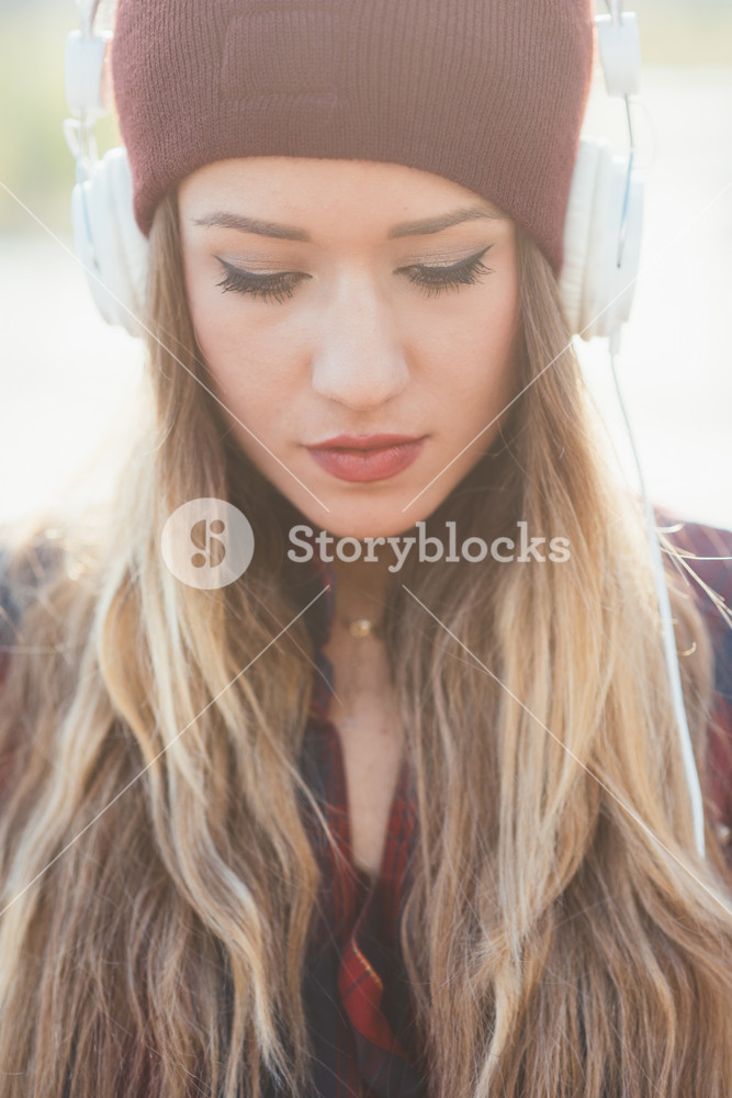 Portrait of a young woman listening to music with headphones, looking down serenely - melancholic, music, relaxing concept