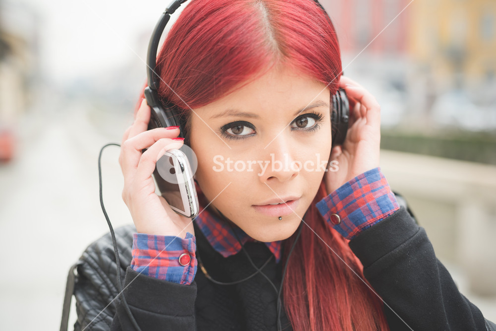Portrait of a young beautiful woman enjoying music outdoors with headphones and a smartphone - music, relaxation, technology concept