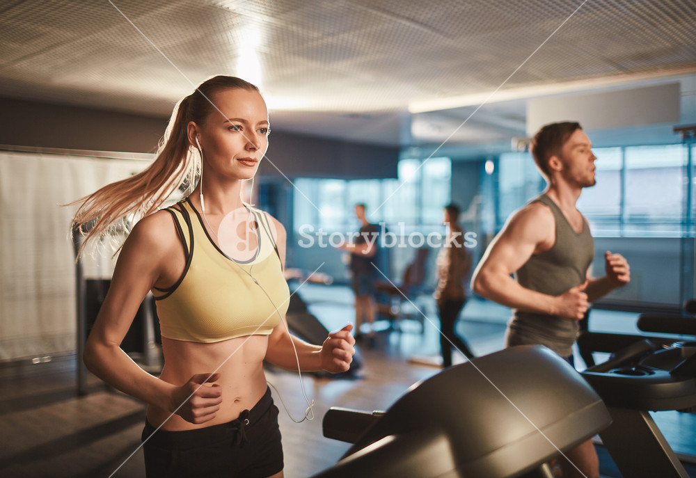 Active woman with earphones enjoying music while running on treadmill