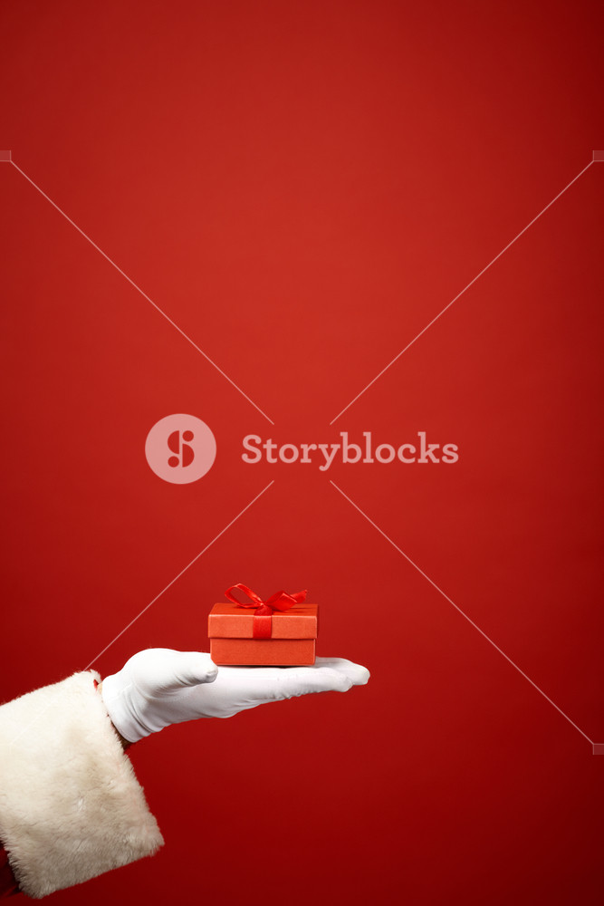 Santa Claus holding a gift with gloved hand on red background Royalty ...