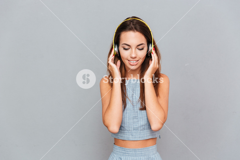 Smiling young woman in headphones enjoying music over grey background