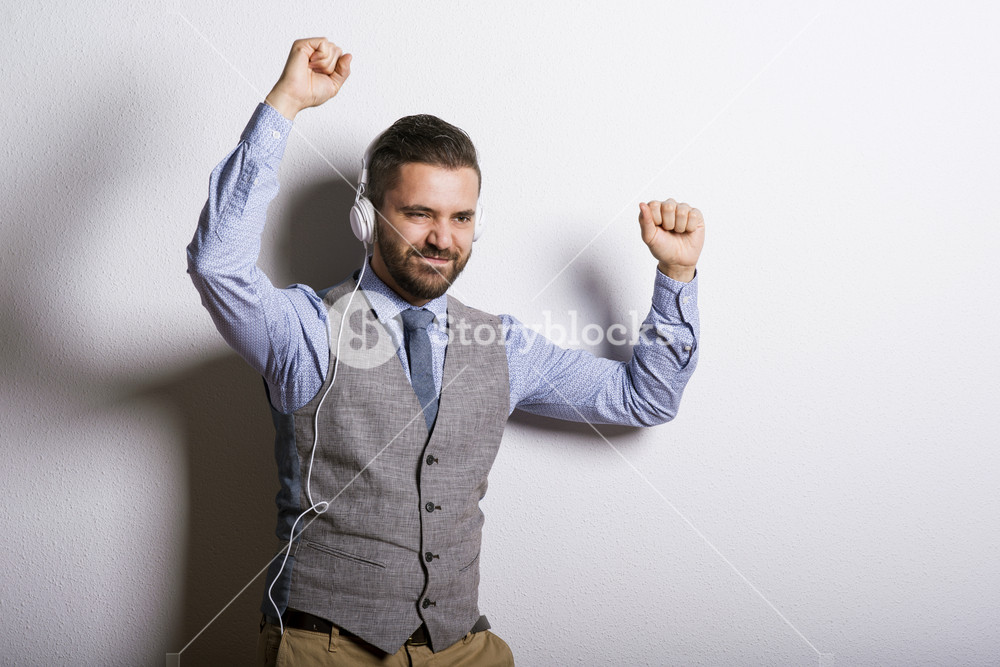 Studio shot of modern hipster businessman with headphones, listening to music and dancing