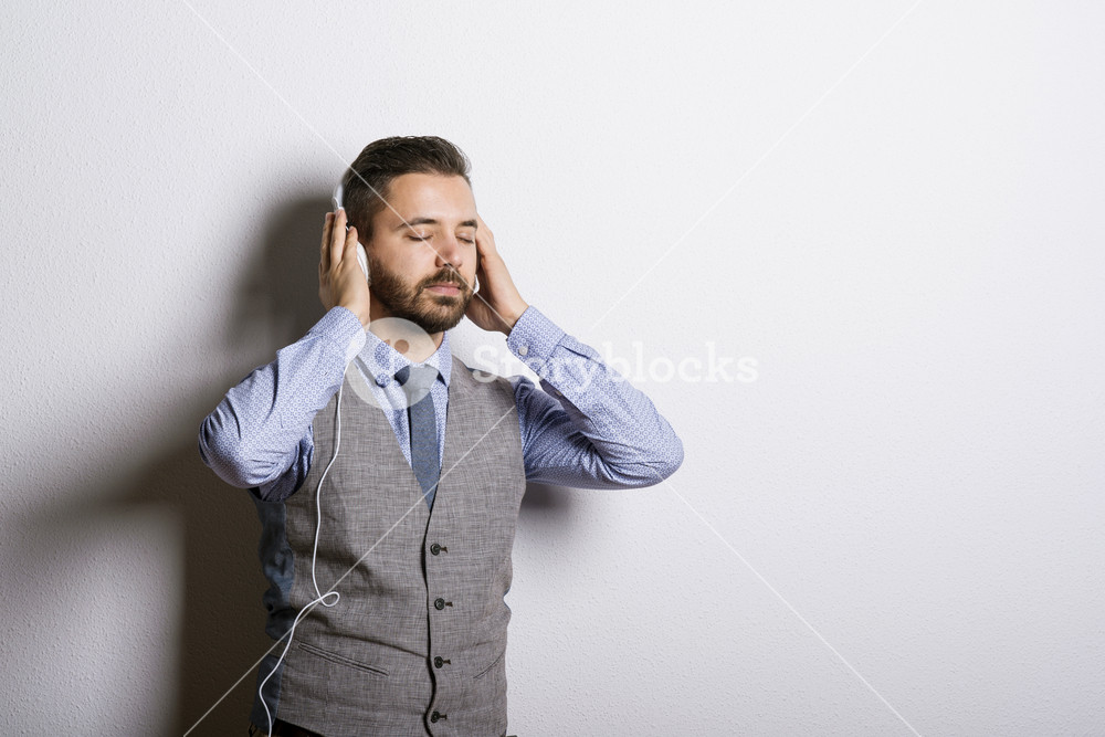 Studio shot of modern hipster businessman with headphones, listening to music