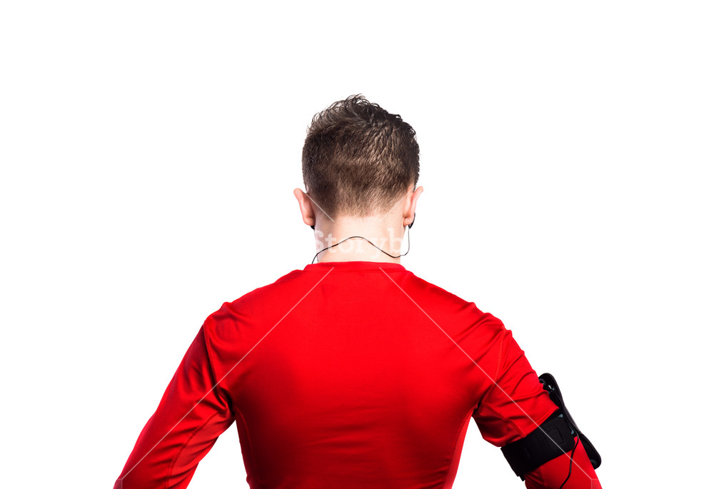 Young boy in red sports sweatshirt with earphones, enjoying music. Handsome youth wearing phone armband. Studio shot on white background, isolated. Rear view.