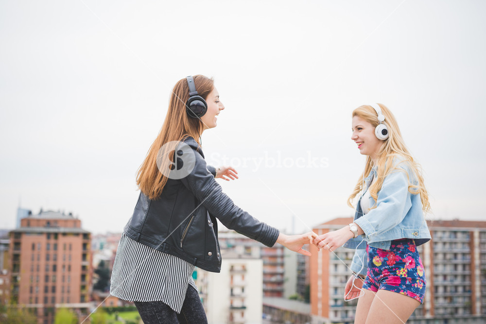 Two young girls enjoying music and friendship in the city - music, technology, friendship concept