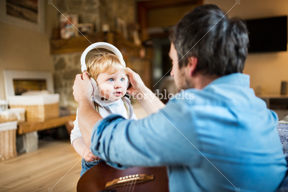 Unrecognizable father at home with guitar, son listening to music.