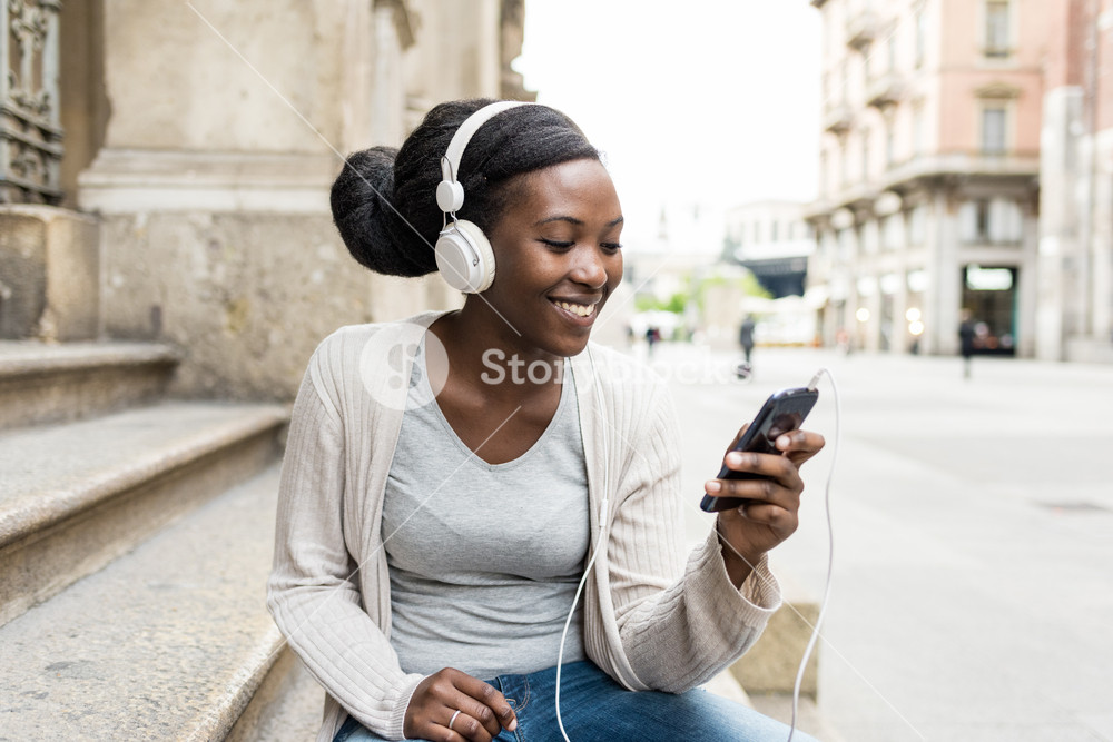 Young woman enjoying music outdoors with headphones and smartphone, smiling - relaxation, happiness, technology concept