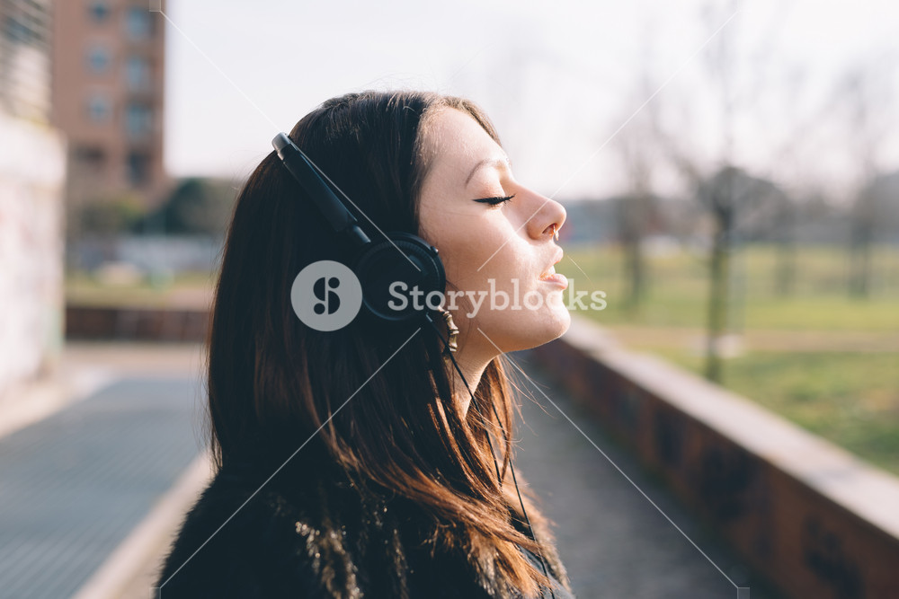 Young woman enjoying music with headphones in a city park - music, relaxation, serenity concept