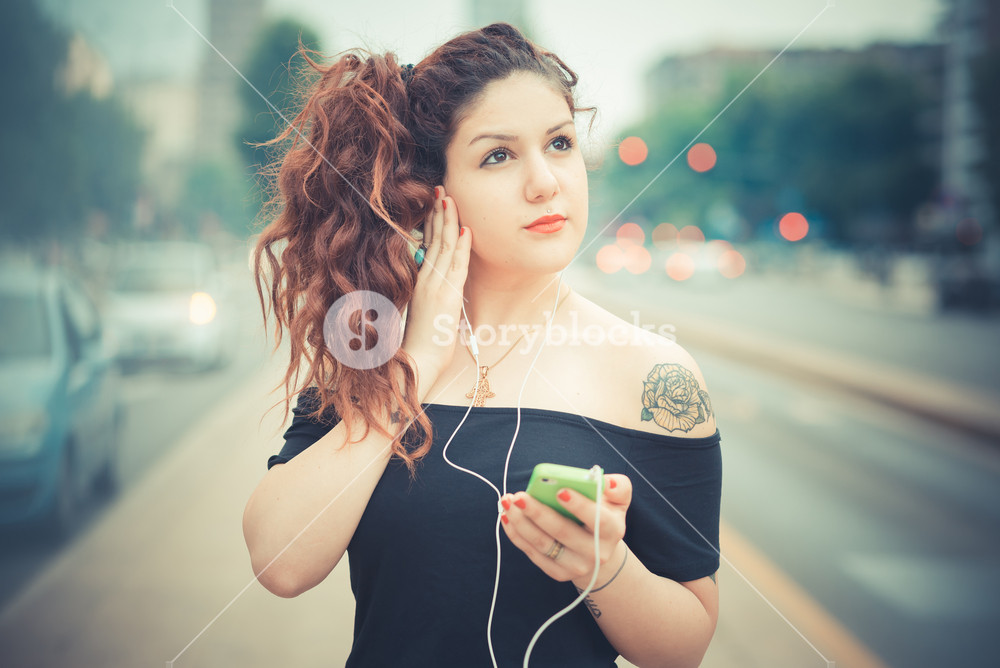 Stylish woman with red curly hair enjoying music in the city