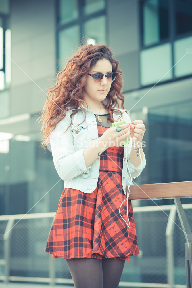 Stylish woman with red curly hair enjoying music in the city