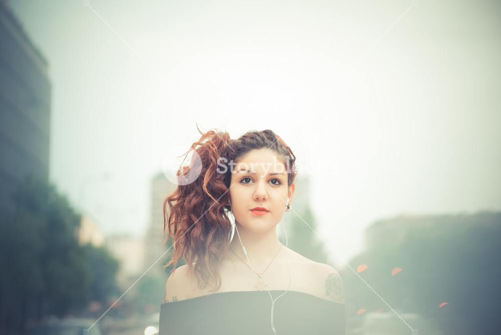 Stylish woman with red curly hair enjoying music in the city