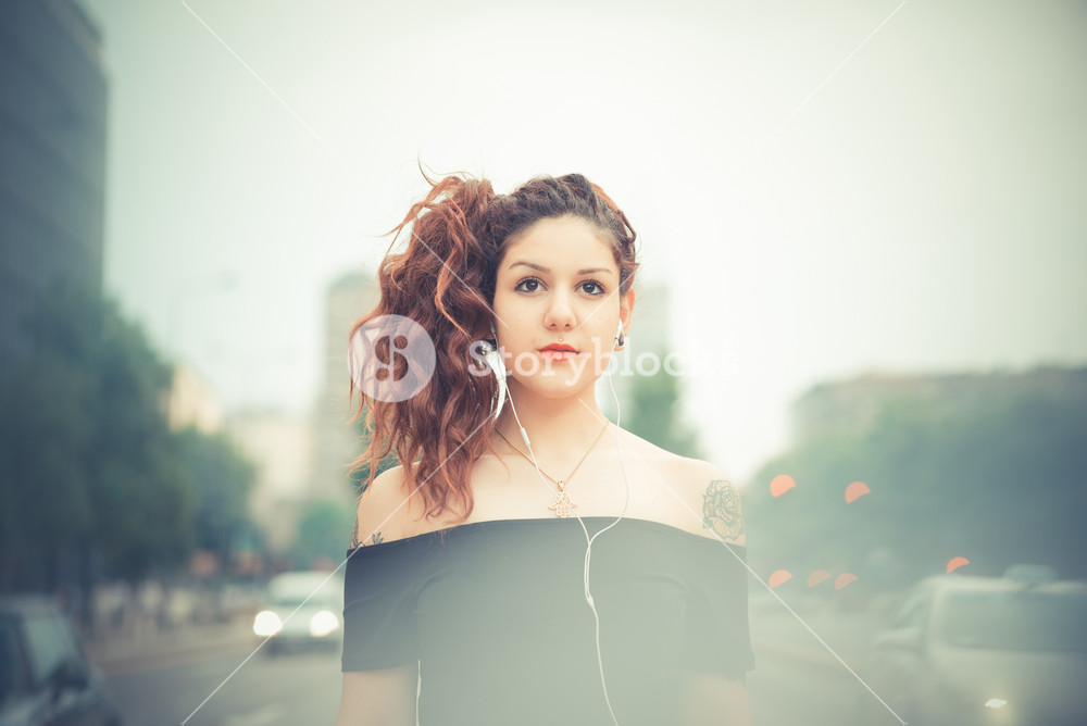 Stylish woman with red curly hair enjoying music in the city