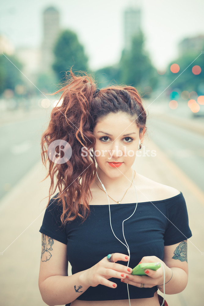 Stylish woman with red curly hair enjoying music in the city