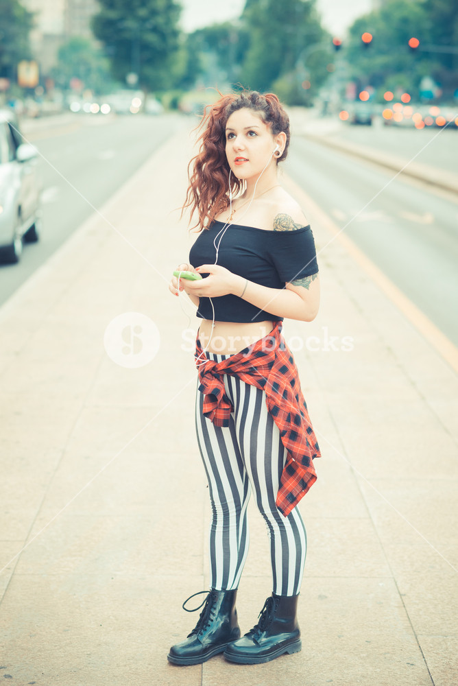 Stylish woman with red curly hair enjoying music in the city