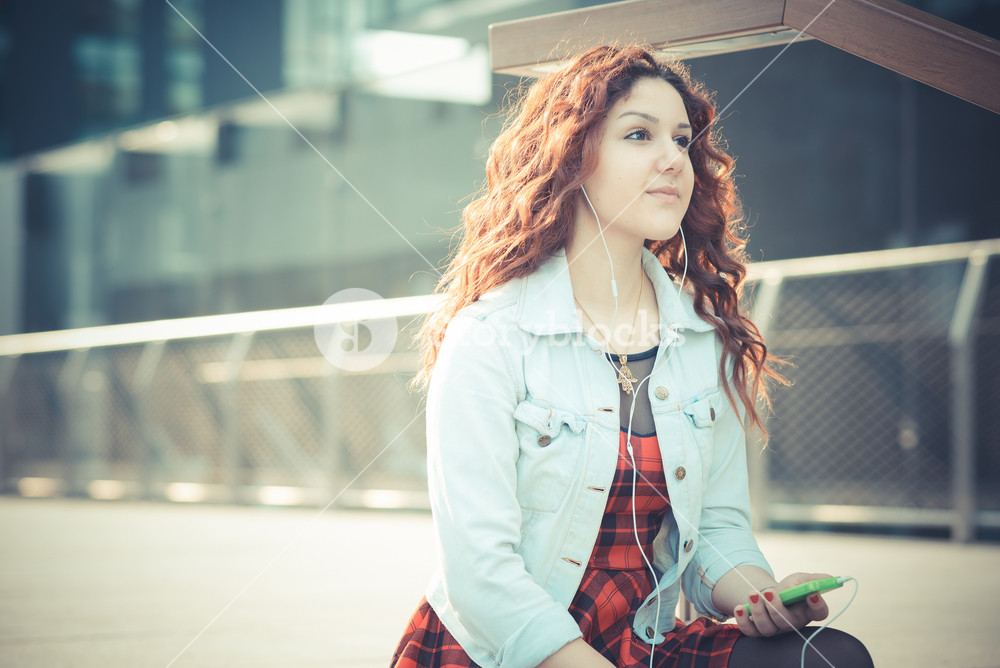 Stylish woman with red curly hair enjoying music in the city
