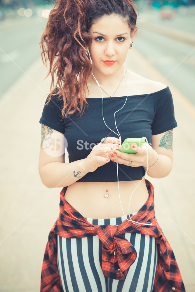 Stylish woman with red curly hair enjoying music in the city