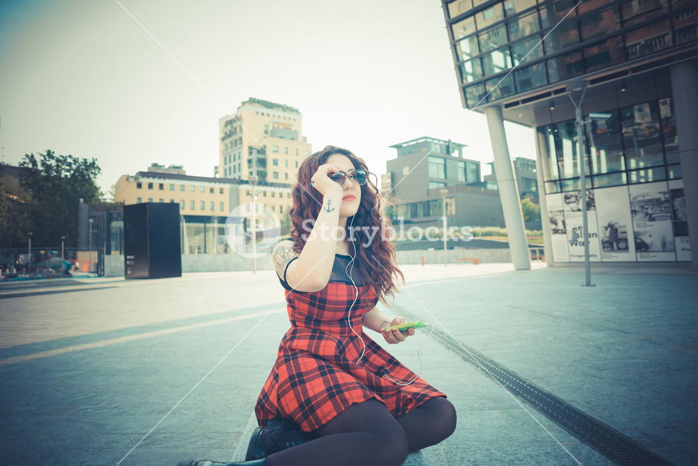 Stylish woman with red curly hair enjoying music in the city