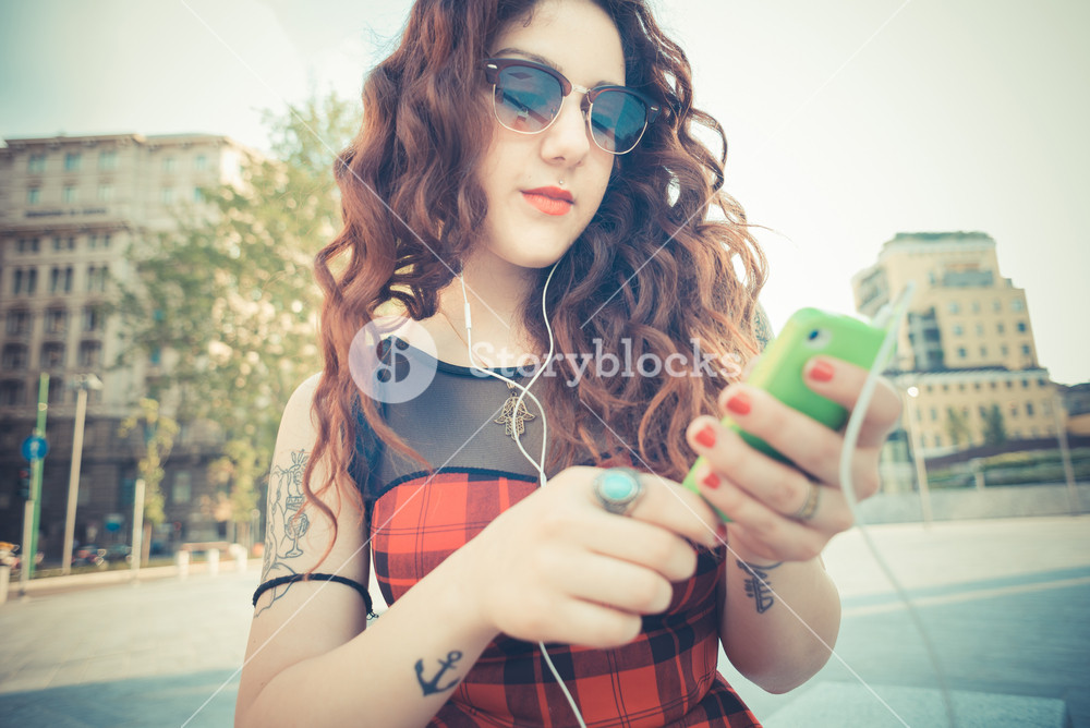 Stylish woman with red curly hair enjoying music in the city