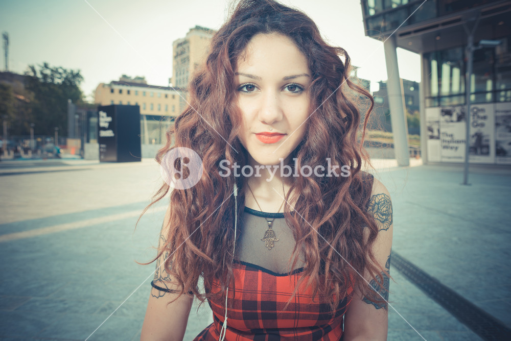 Stylish woman with red curly hair enjoying music in the city
