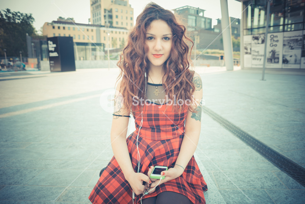 Stylish woman with red curly hair enjoying music in the city
