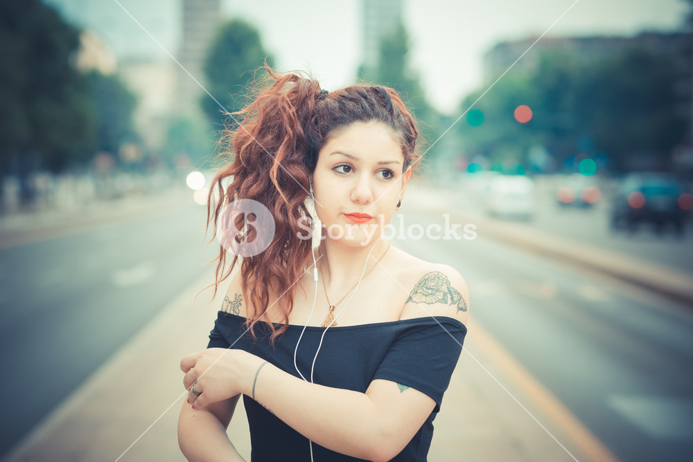 Stylish woman with red curly hair enjoying music in the city