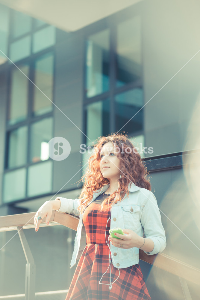 Stylish woman with red curly hair enjoying music in the city