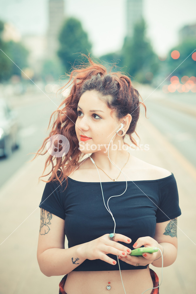 Stylish woman with red curly hair enjoying music in the city