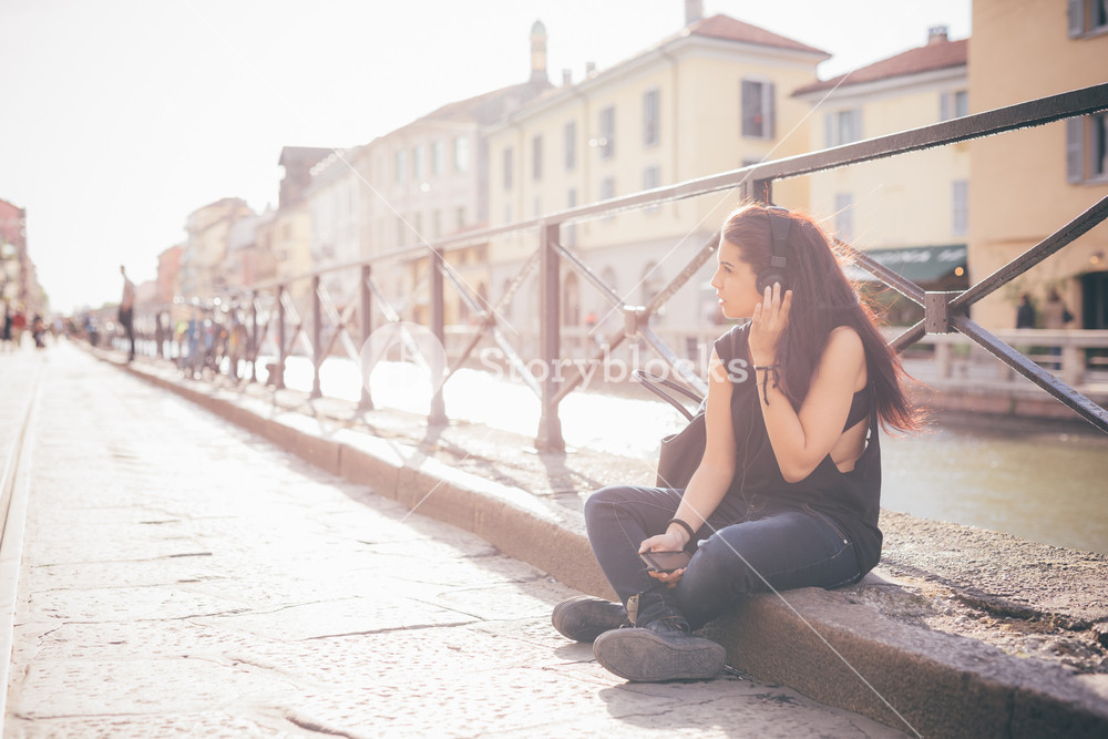 Young woman enjoying music on the sidewalk - relaxation, music, technology concept - wearing black shirt, looking to the right