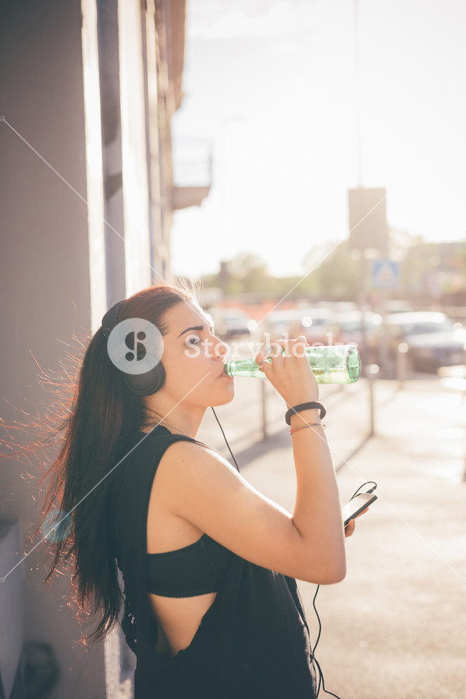 Young woman enjoying music while walking through the street - relaxation, music, technology concept - wearing black shirt, holding beverage