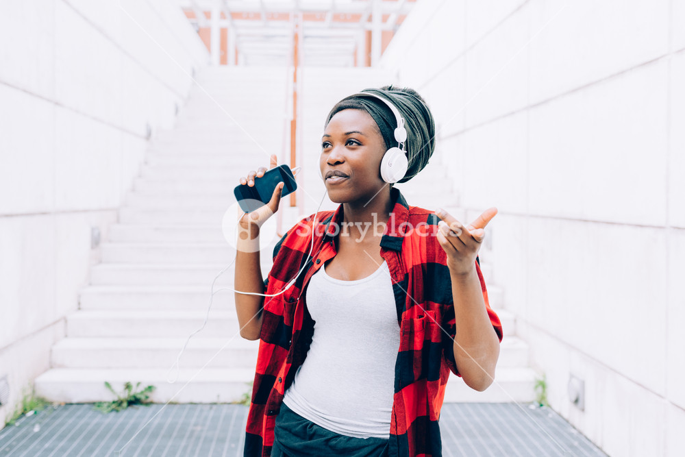 Young woman enjoying music with headphones and smartphone, dancing outdoors in the city, smiling - happiness, serene, technology concept