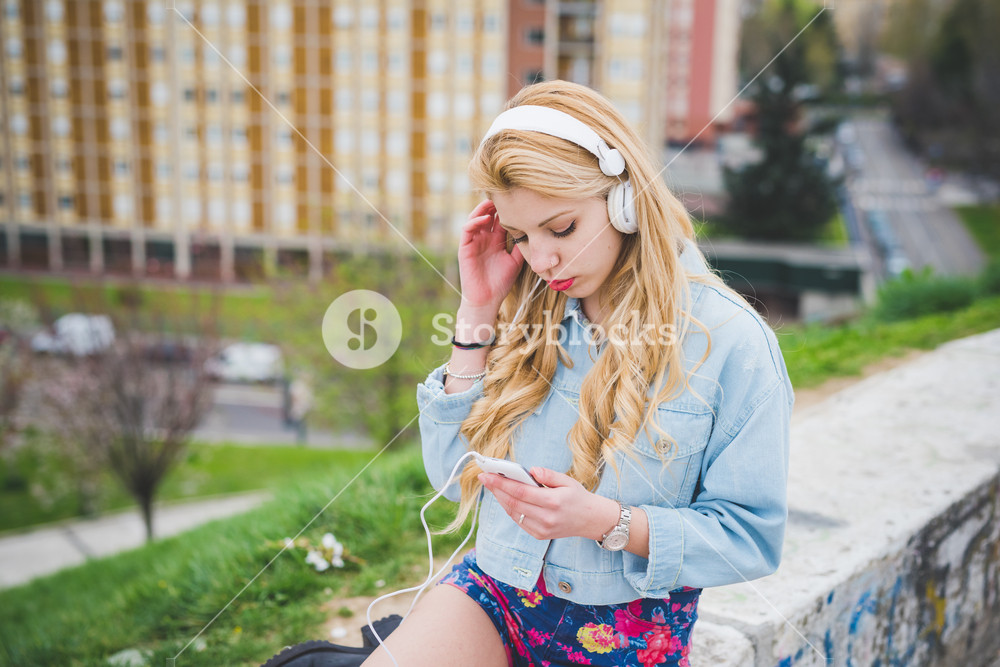 Blonde girl enjoying music with headphones and smartphone in the suburbs - technology, music, relaxation concept