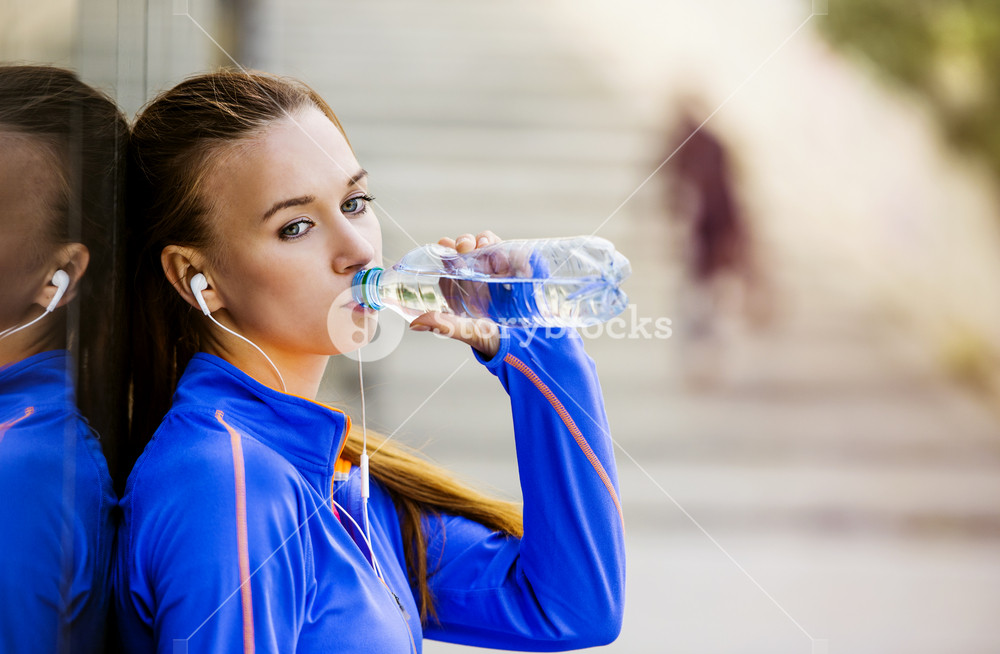 Young runner takes a break, hydrates, and enjoys music in the city center